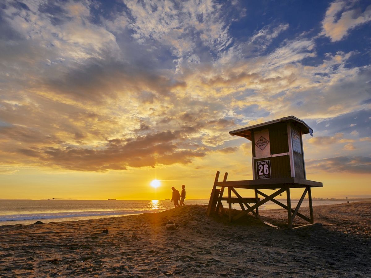 A beach scene at sunset features a lifeguard tower marked 