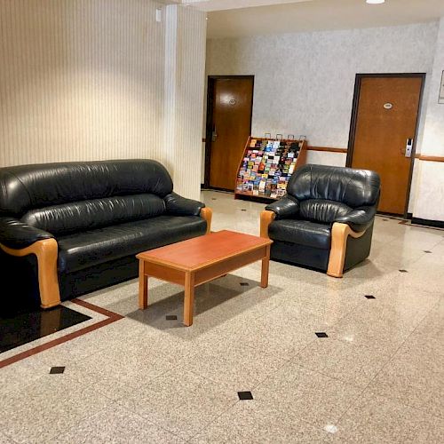 A lobby area with two black leather sofas, a wooden coffee table, a magazine rack, and two closed doors in the background.