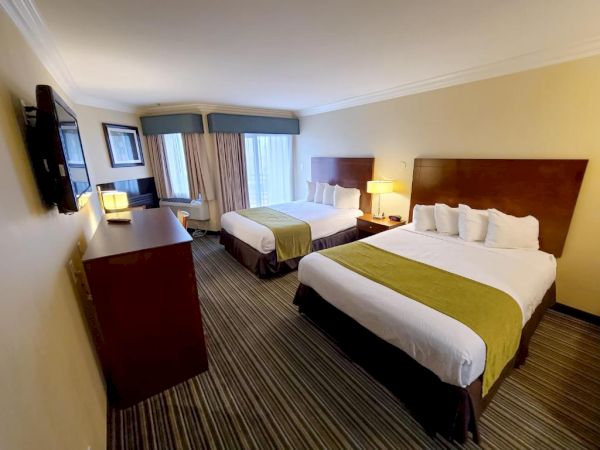 A hotel room with two double beds, a dresser, a TV, a chair by the window, and bedside lamps, all in a well-lit and neatly arranged setting.