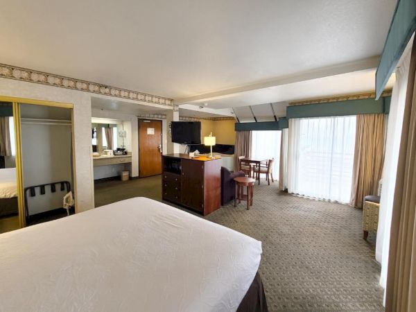 A hotel room with a bed, TV, dresser, table and chairs, closet with mirrored doors, and a large window with curtains.