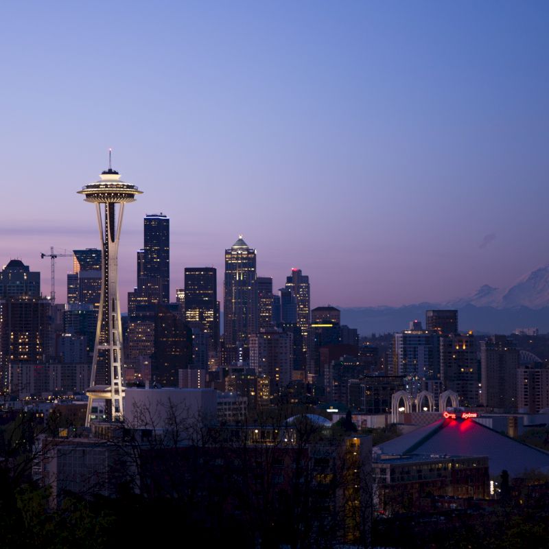 The image shows the Seattle skyline during dusk, featuring the Space Needle and city buildings, with Mount Rainier visible in the background.