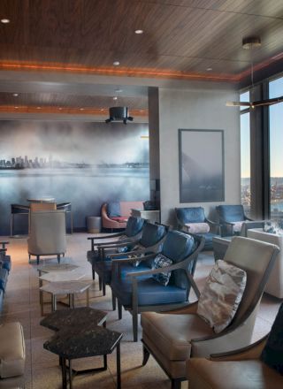 A modern lounge area with multiple chairs and tables, a wall mural of a cityscape, and large windows with a scenic ocean view, ending the sentence.