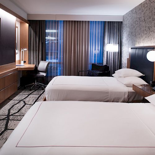 A modern hotel room with two neatly made twin beds, a flat-screen TV, a work desk with a chair, and contemporary decor, ending the sentence.