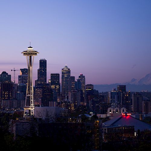 This image shows a view of Seattle's skyline at dusk, including the Space Needle and Mt. Rainier in the background.