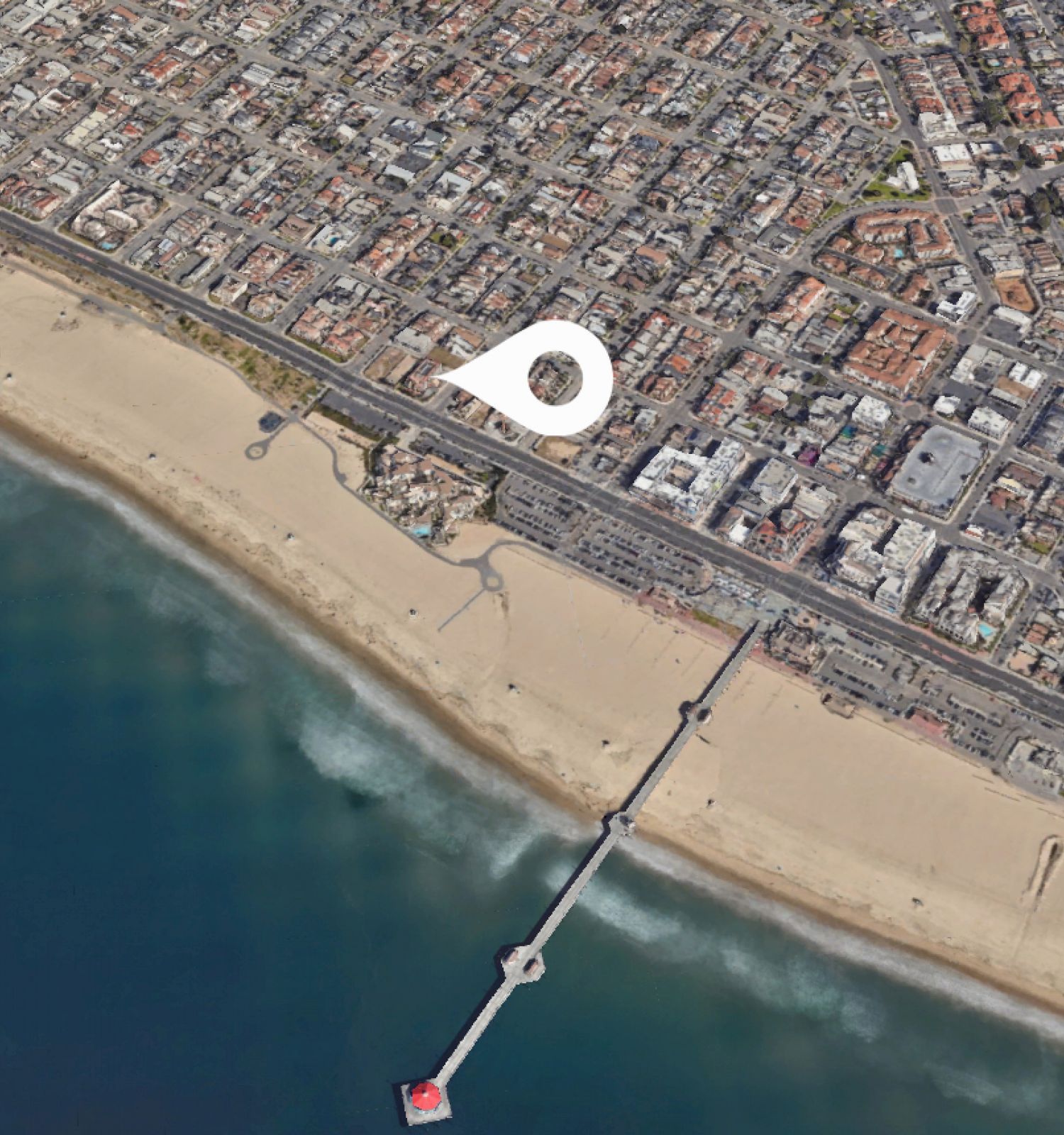 This image shows an aerial view of a coastal city with a long pier extending into the ocean from a sandy beach, and a map marker icon above the city.